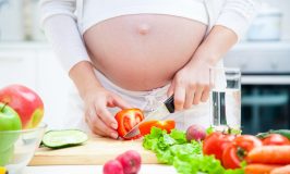 Pregnant woman in kitchen making salad
